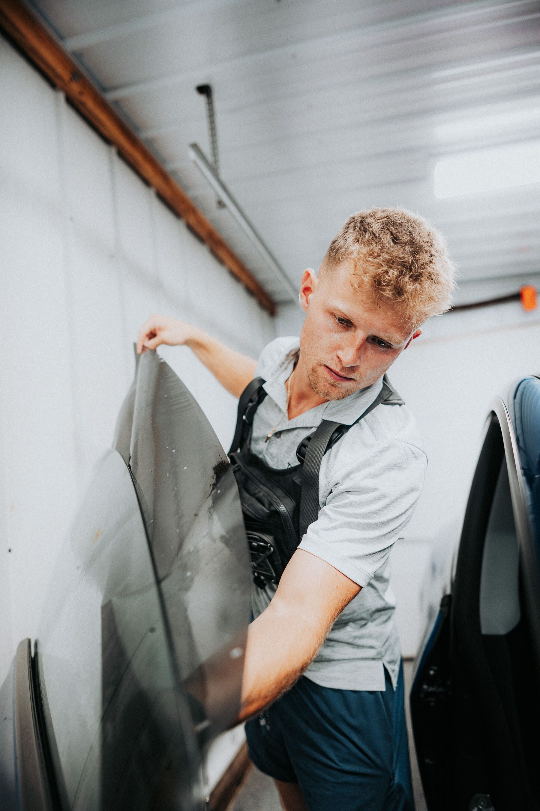 Person lifting a black panel in a workshop or warehouse, wearing a white shirt and dark overalls.