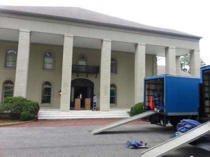 Moving trucks parked at the front of a two-story building with large columns.