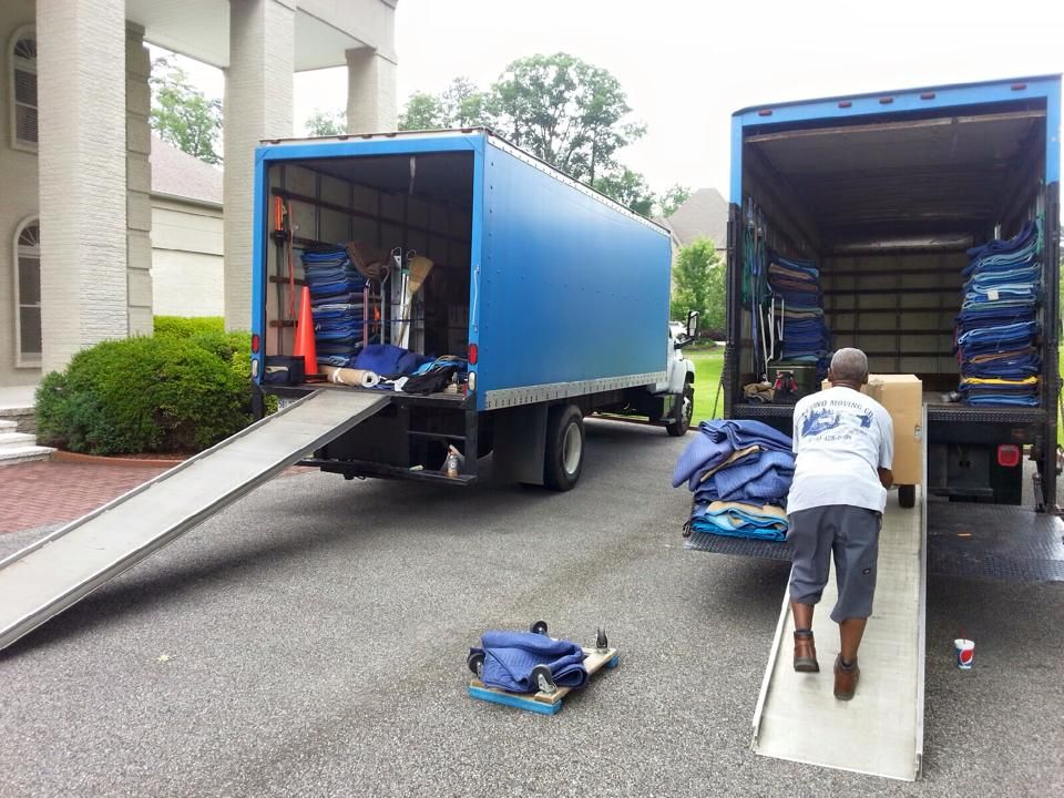 Two blue moving trucks parked in a driveway; movers loading boxes.