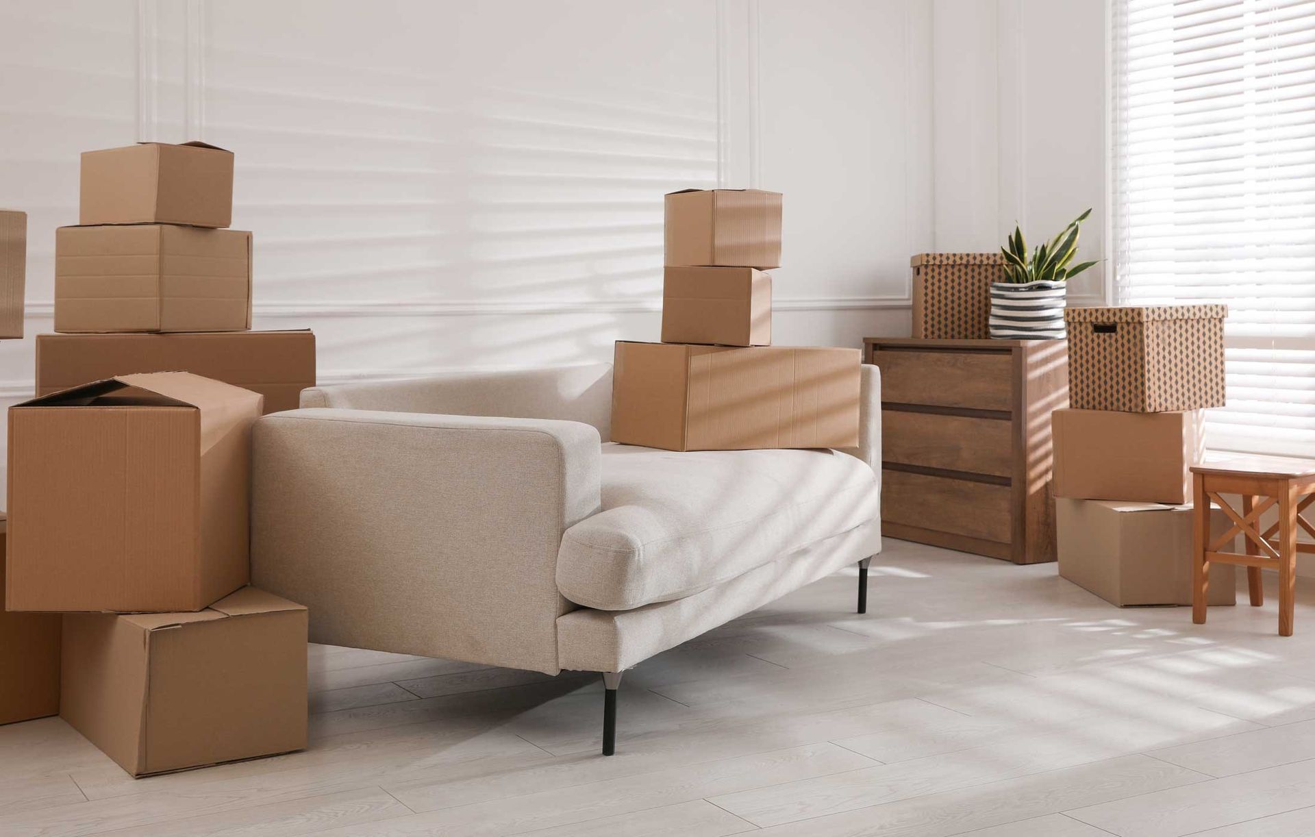 Boxes stacked around a neutral-toned couch in a bright room; moving day.