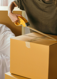 Person seals a cardboard box with tape, likely packing for a move.