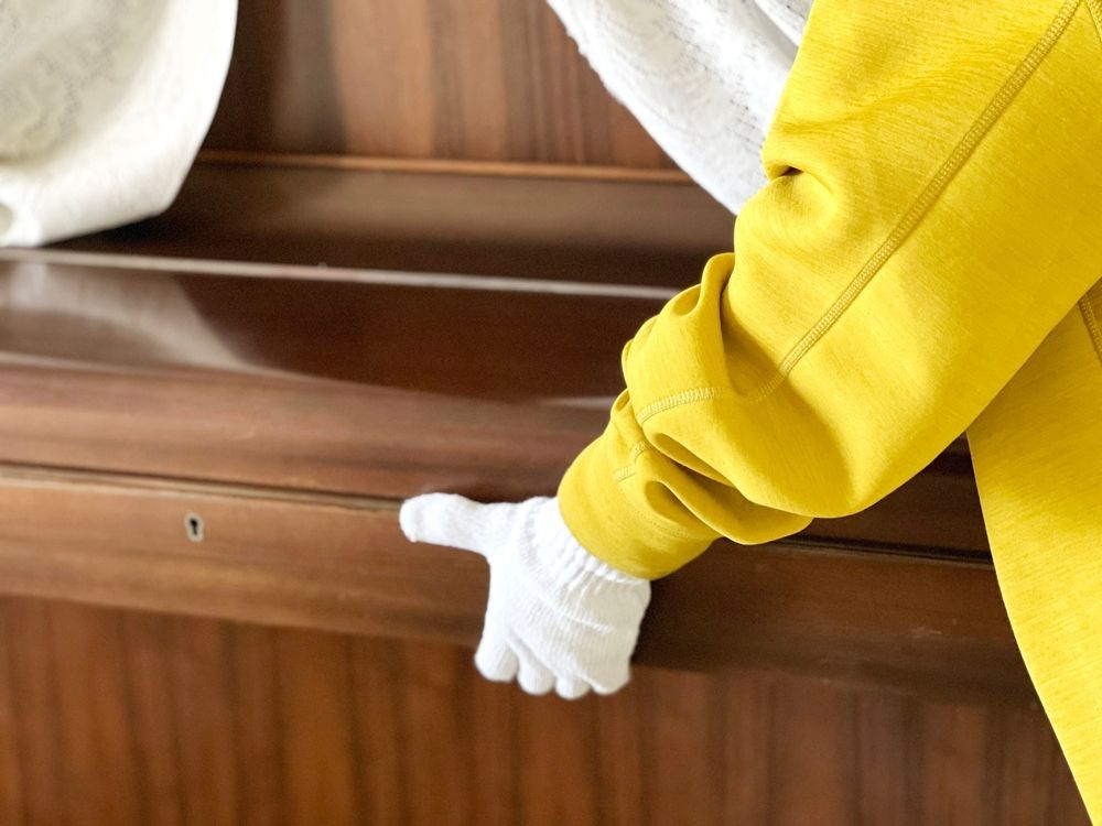 Person in yellow jacket and white glove opens a piano.