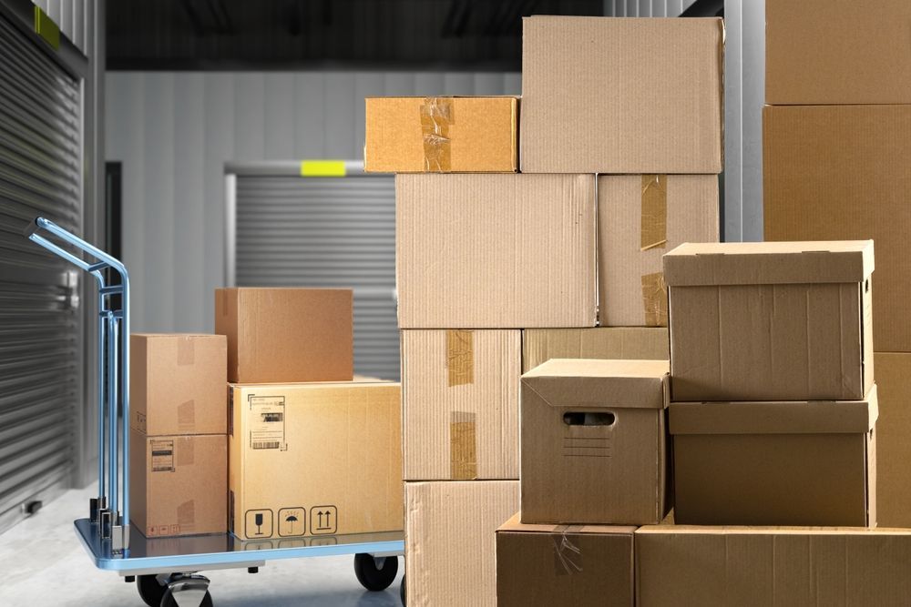 Boxes stacked on a hand truck and in a storage unit; moving.