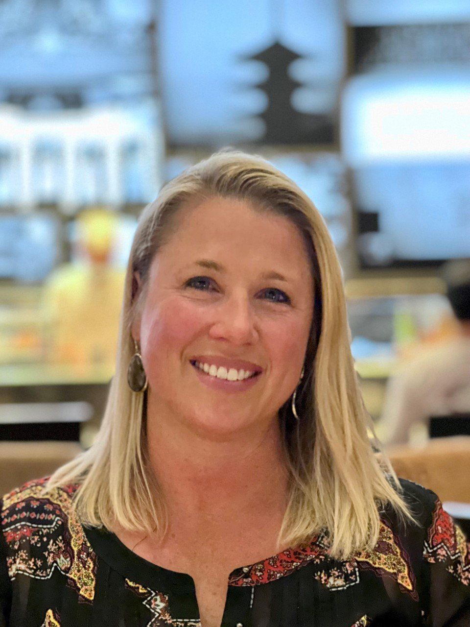 A woman with blonde hair is smiling for the camera in a restaurant.