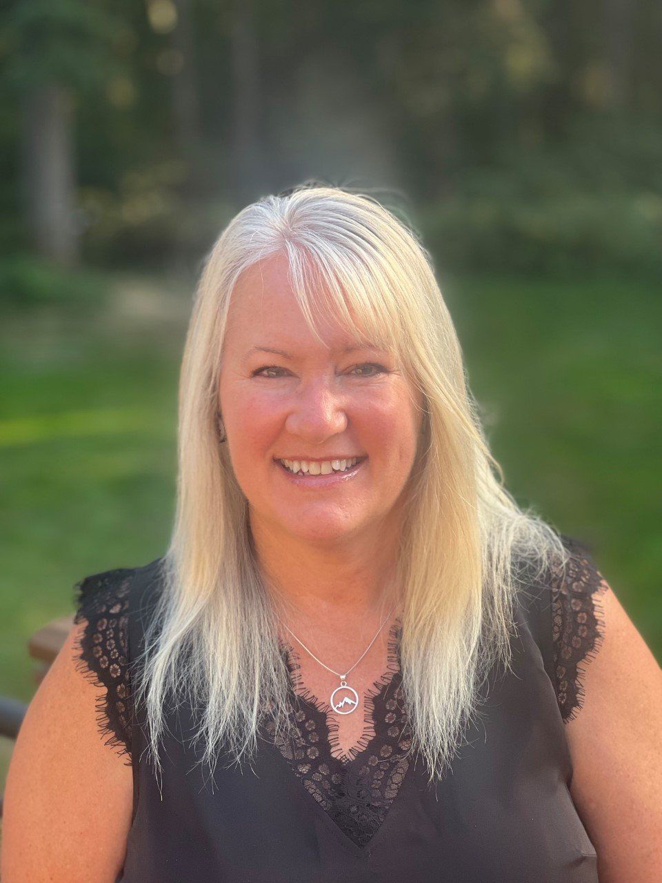 A woman wearing a black shirt and a necklace is smiling for the camera.
