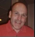 A bald man wearing a red shirt is smiling for the camera.