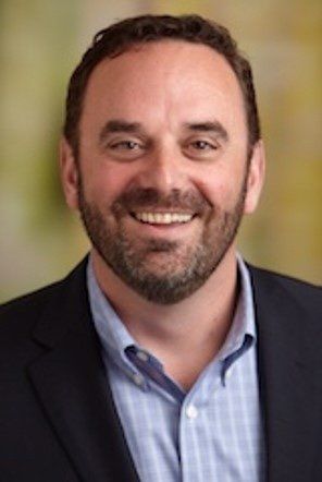 A man with a beard is wearing a suit and smiling.