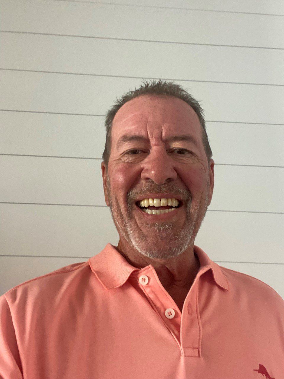 A man wearing a pink polo shirt is smiling for the camera.