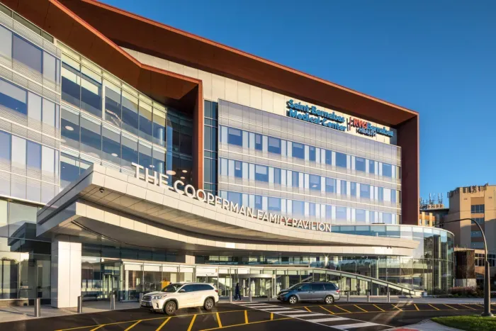 Modern hotel exterior with curved glass facade, parked cars, and blue sky