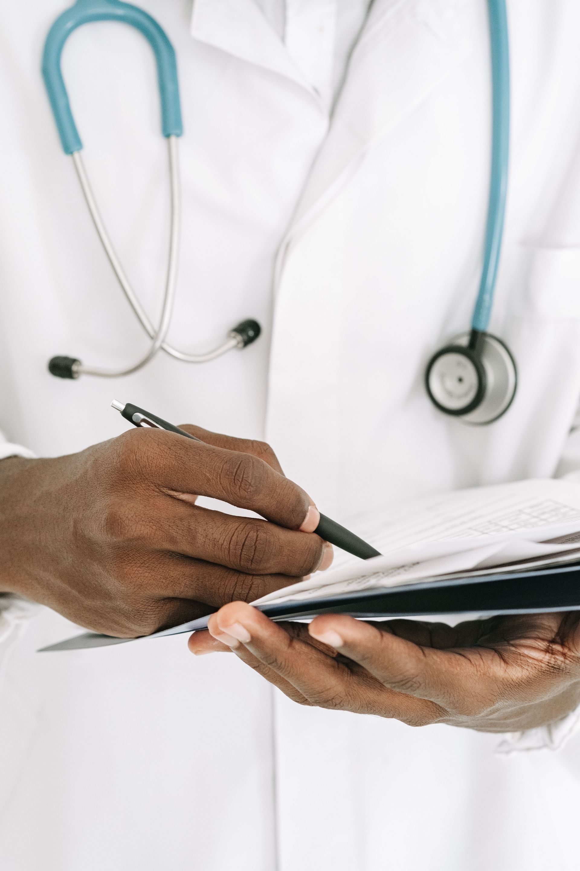 Doctor writing on a clipboard with a blue stethoscope around the neck.