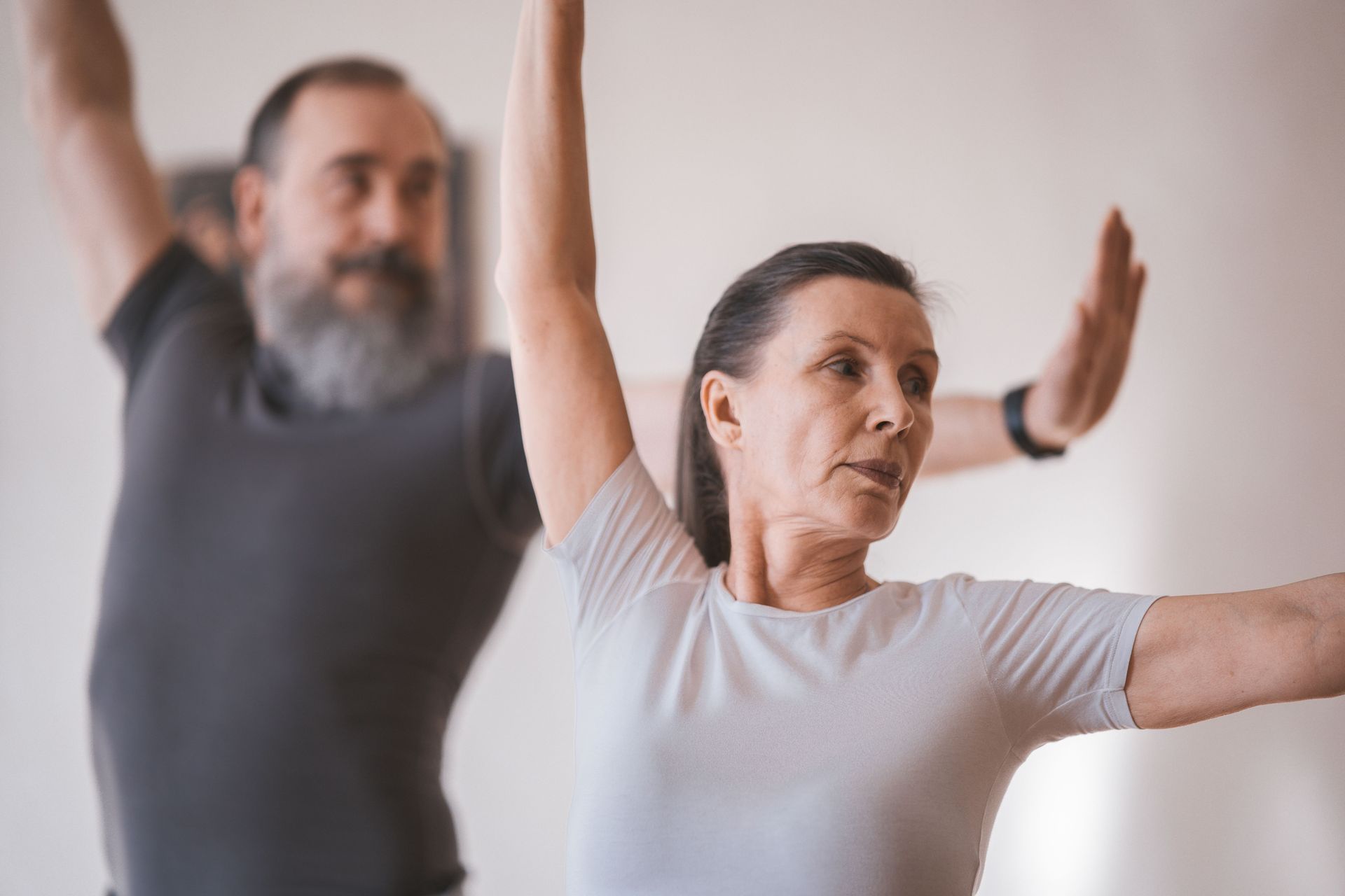 Two people stretching with raised arms in a bright indoor exercise class