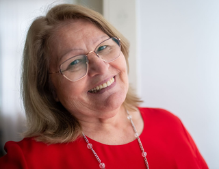 Smiling woman in a red top and glasses, wearing a silver necklace, against a softly blurred background