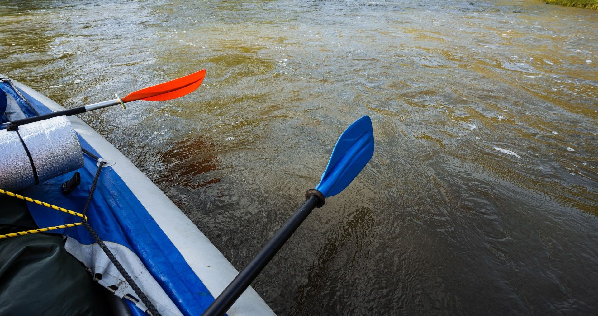 Two paddles, orange and blue, over churning water from a raft.