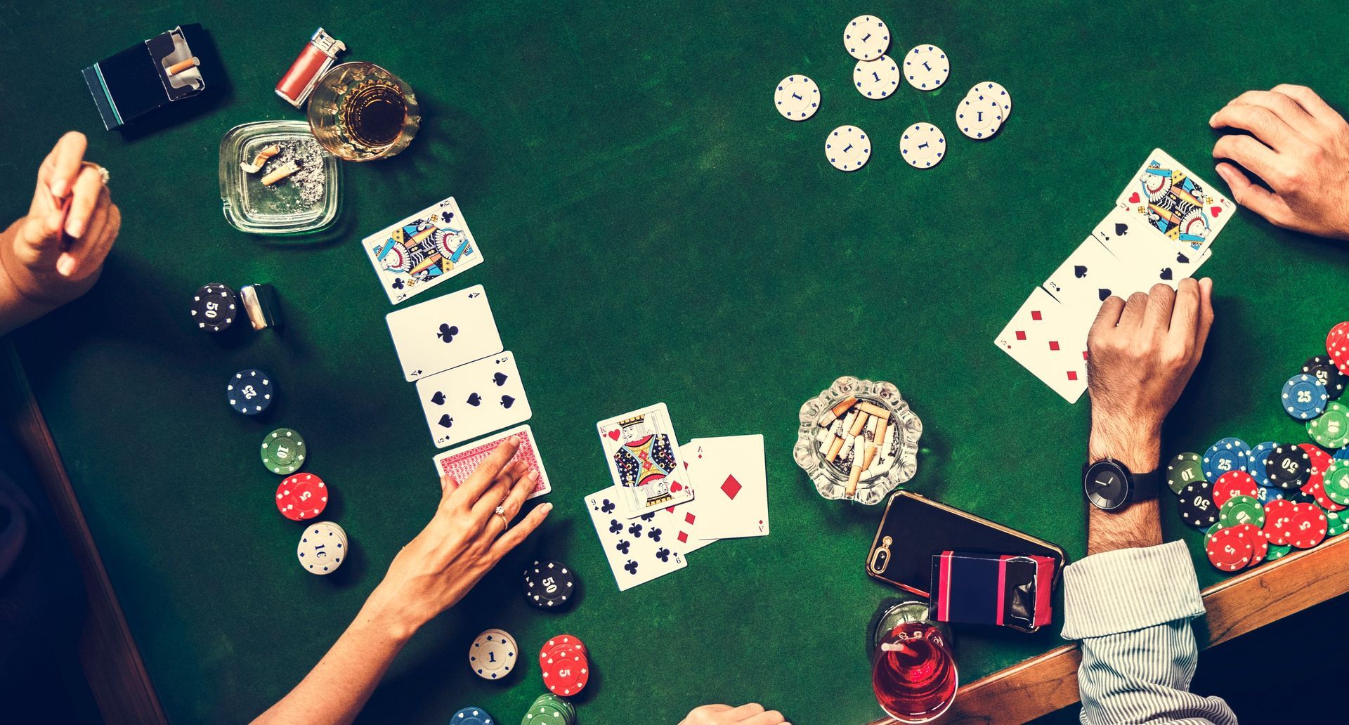 Poker game in progress; hands visible on a green table, cards, chips, and drinks.