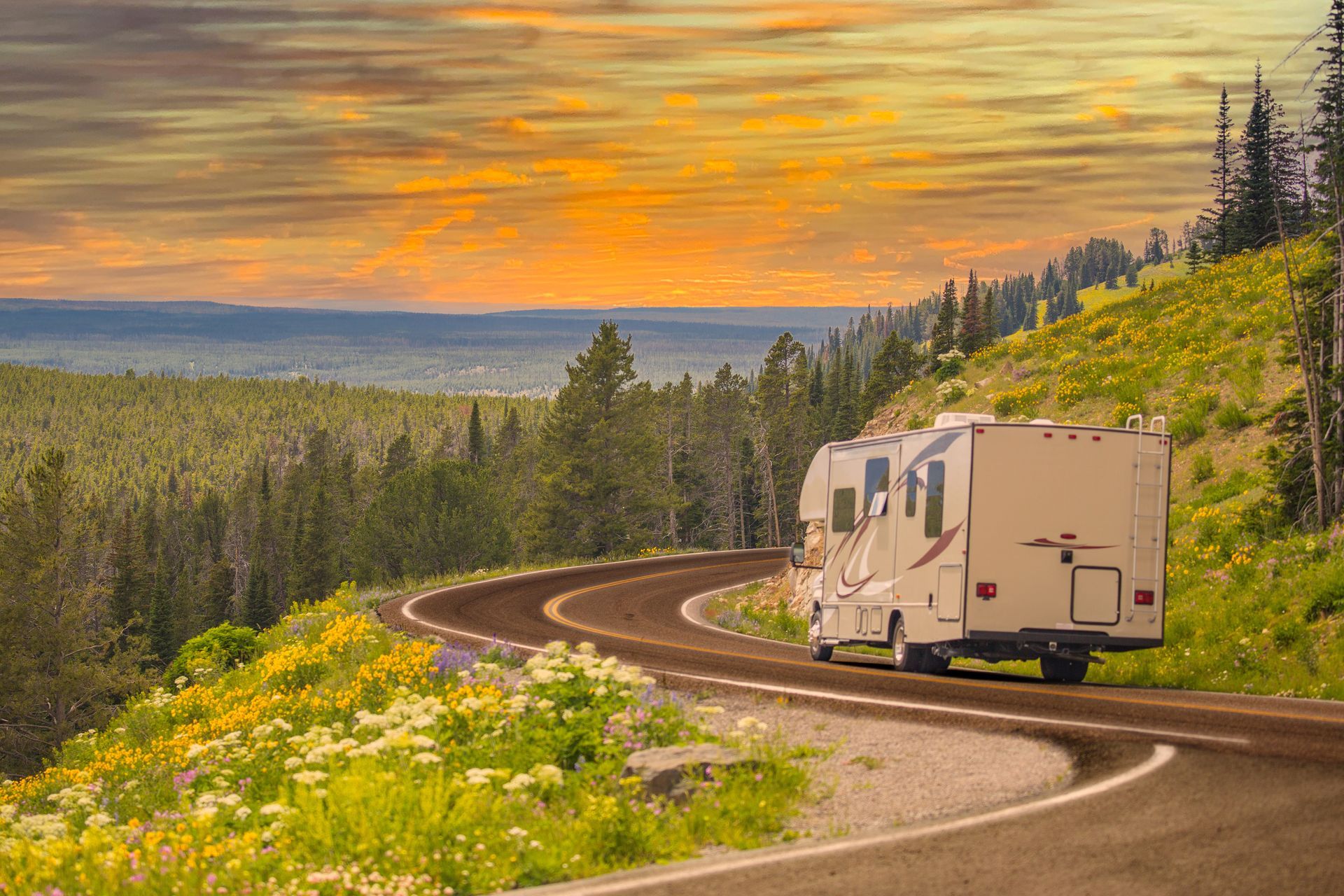 RV on a winding mountain road at sunset, overlooking a forested valley