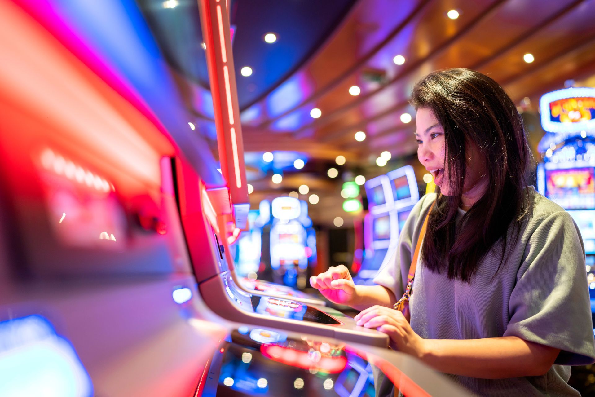 Woman playing a slot machine, illuminated by bright casino lights, showing excited expression.