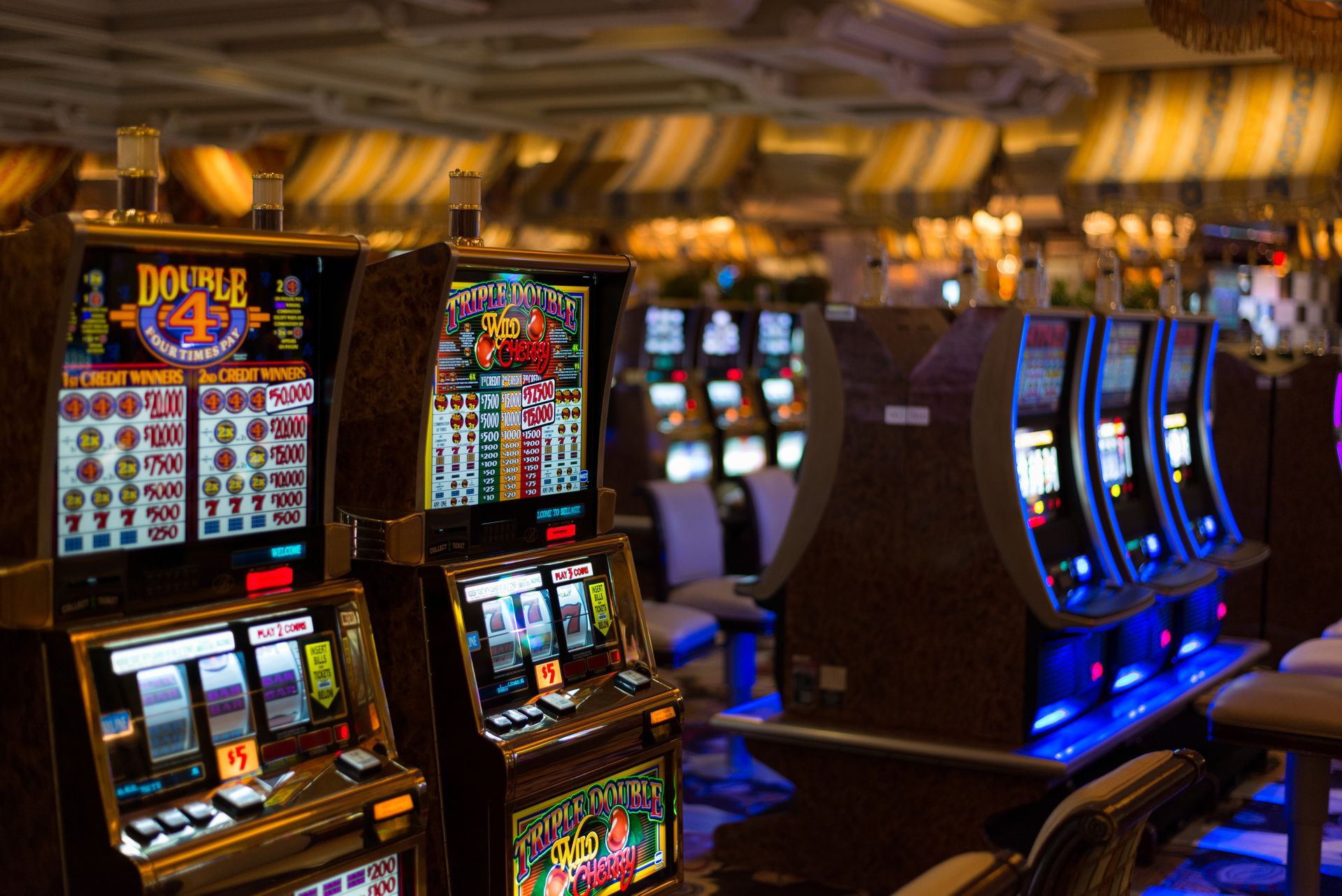 Slot machines in a casino, with colorful screens and bright lights, in a dimly lit setting.