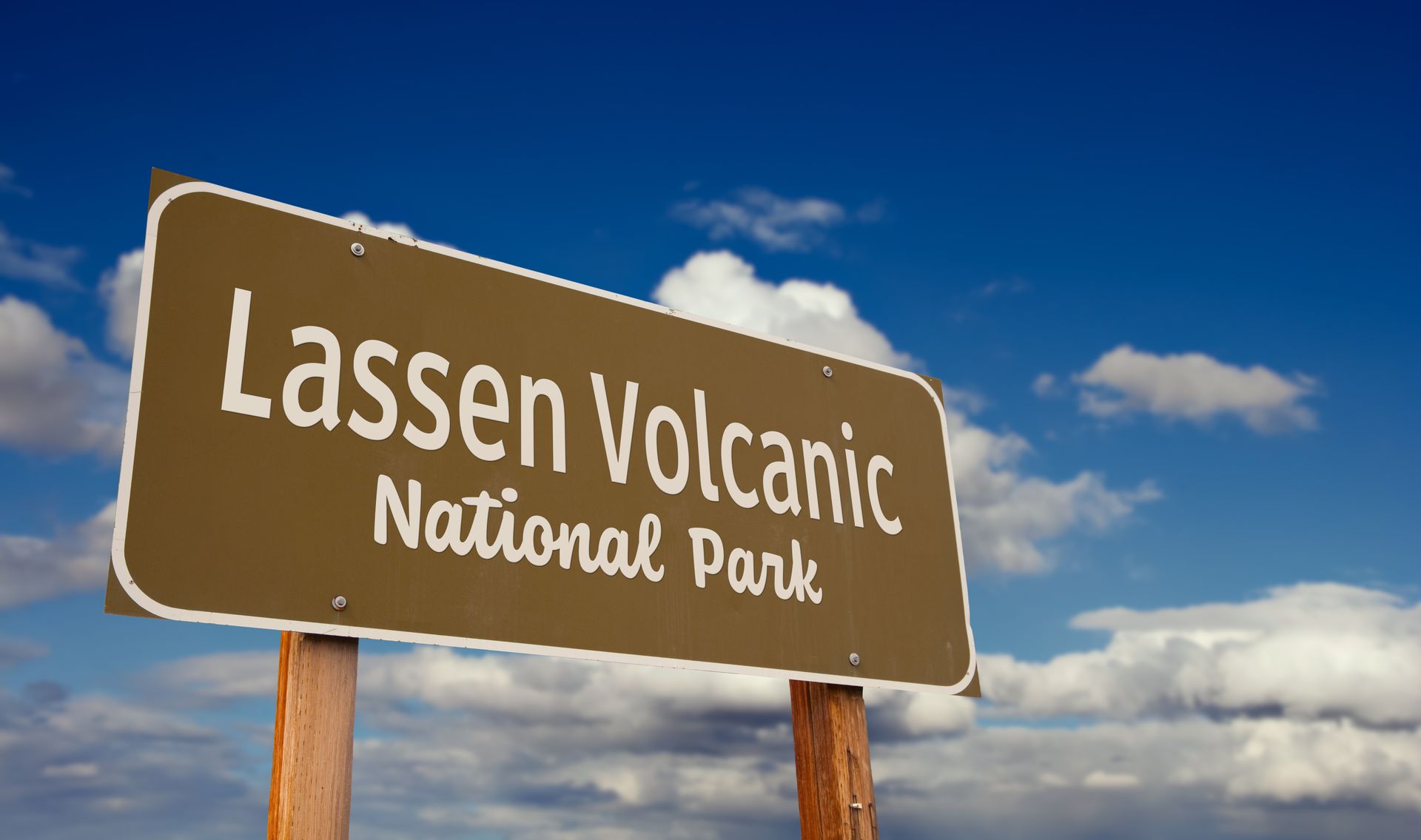 Lassen Volcanic National Park sign with text against a blue, cloudy sky.