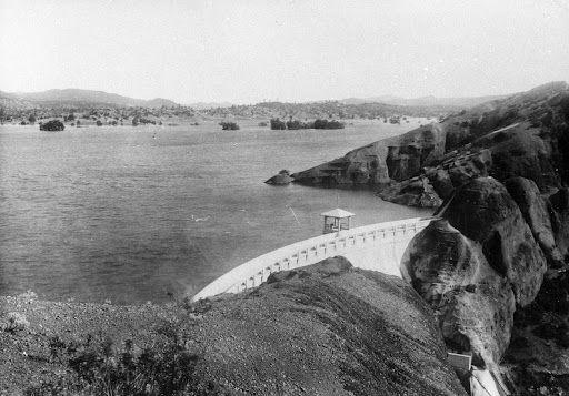 A large concrete dam in a valley, with a lake extending into the background.