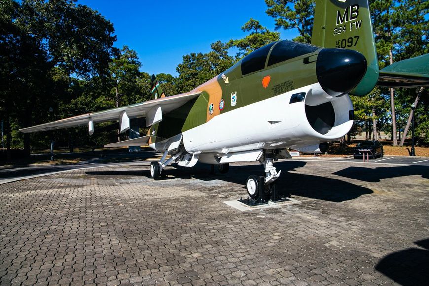 A-7 Corsair II aircraft on display, parked on paved ground with trees in background.