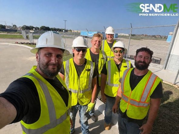 Five construction workers in hard hats and safety vests posing at an outdoor job site.