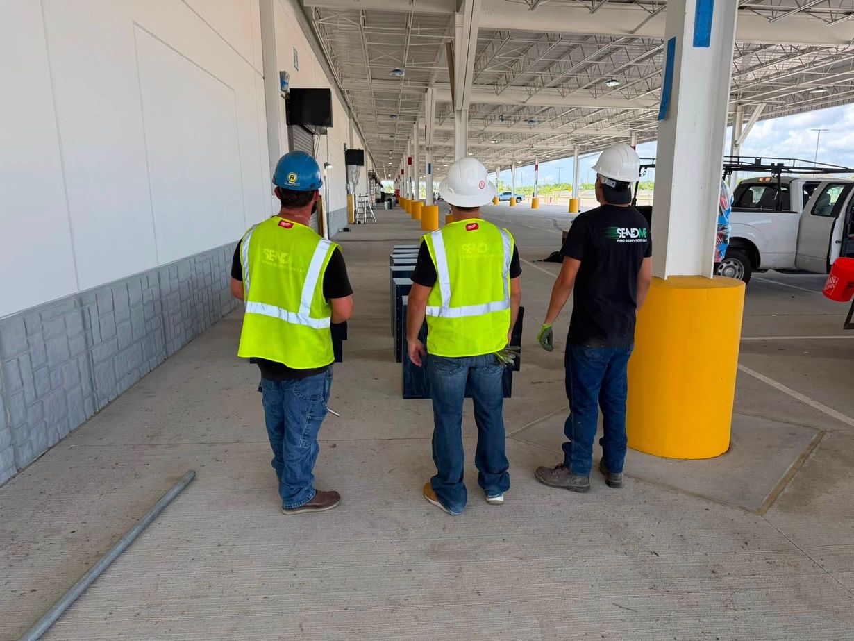 Three workers in hard hats and safety vests walking along a covered industrial walkway