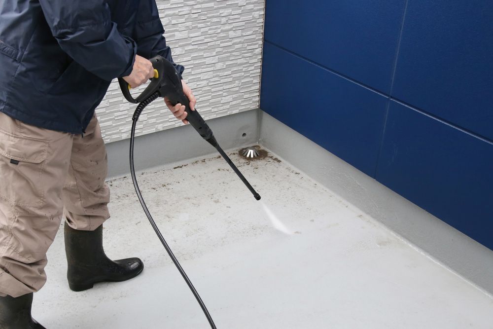 A Man is Cleaning the Floor With a High Pressure Washer — Ryno's Plumbing Group in Lakewood, NSW