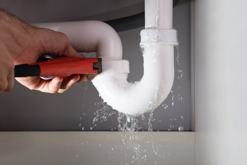 A Person is Fixing a Leaking Sink Pipe With a Wrench — Ryno's Plumbing Group in Laurieton, NSW