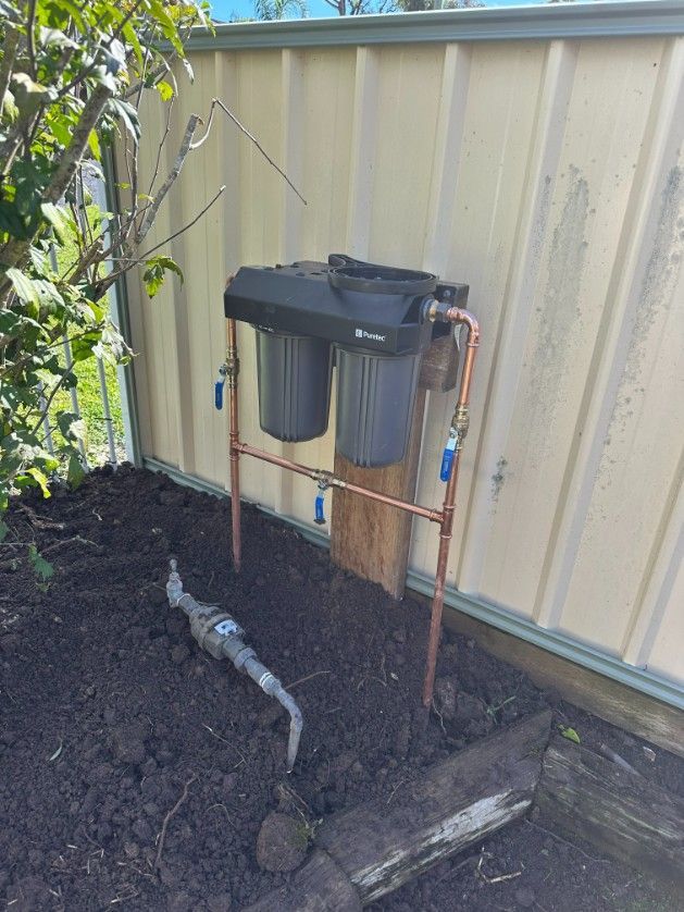 A Water Filter is Sitting in the Dirt Next to a Fence — Ryno's Plumbing Group in Lakewood, NSW