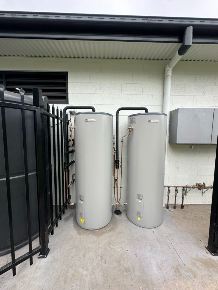 Two Water Heaters Are Sitting Outside of a Building Next to a Black Fence — Ryno's Plumbing Group in Lakewood, NSW