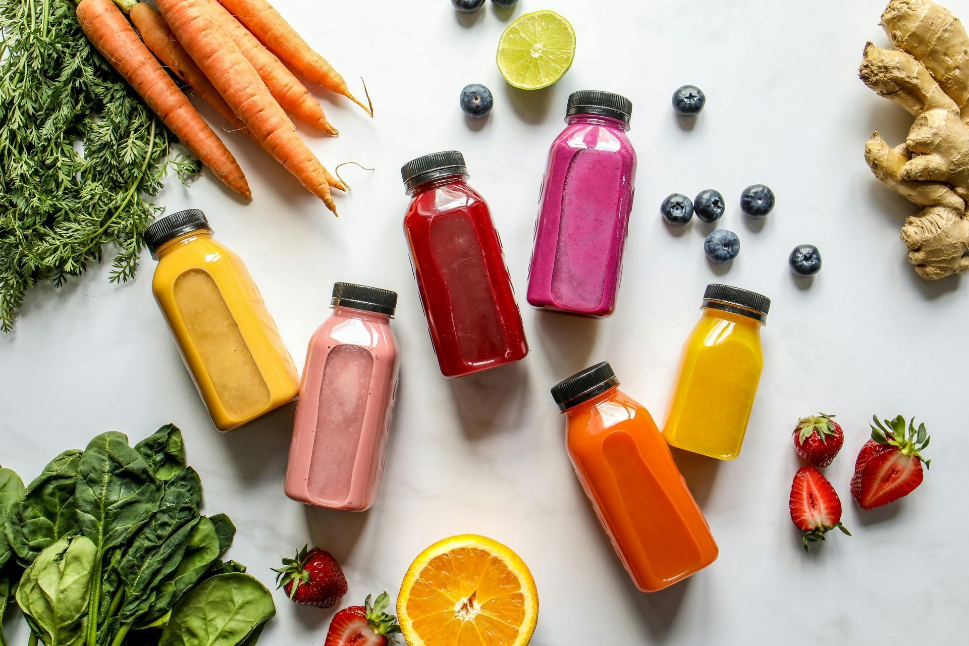Bottles of colorful juice with surrounding fruits and vegetables.