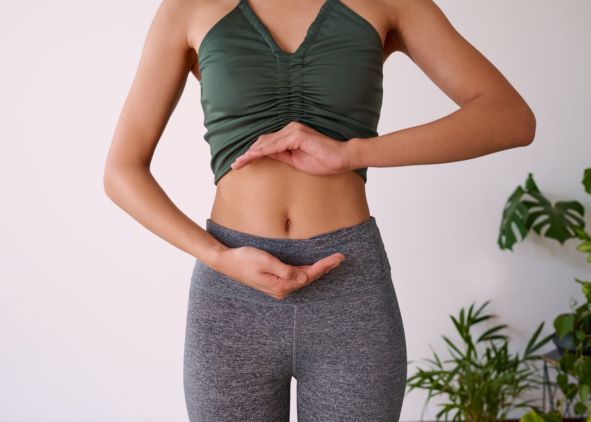 Woman in activewear with hands near abdomen, possibly practicing yoga indoors.