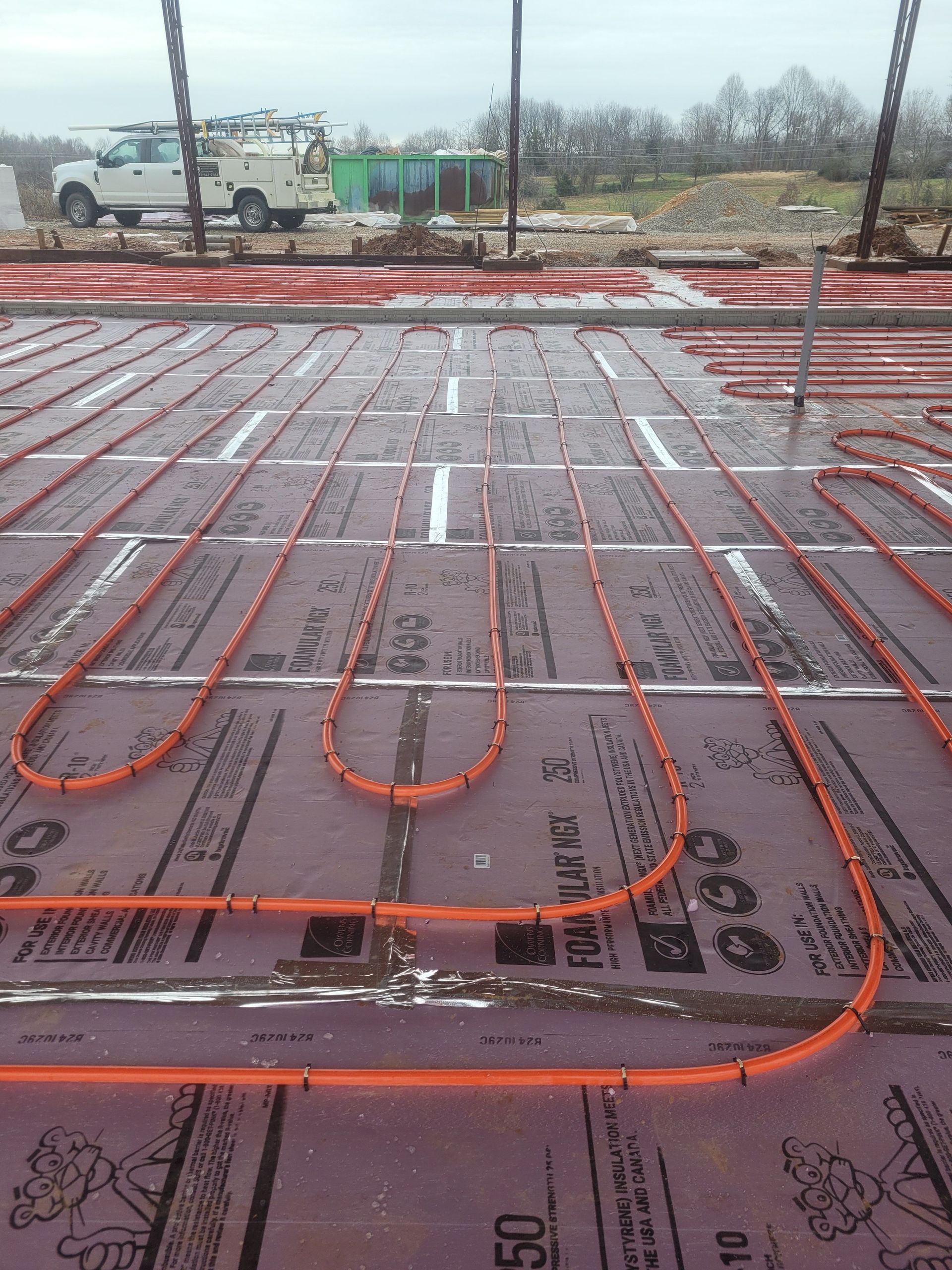 Orange heating tubes laid across purple insulation on a construction site.
