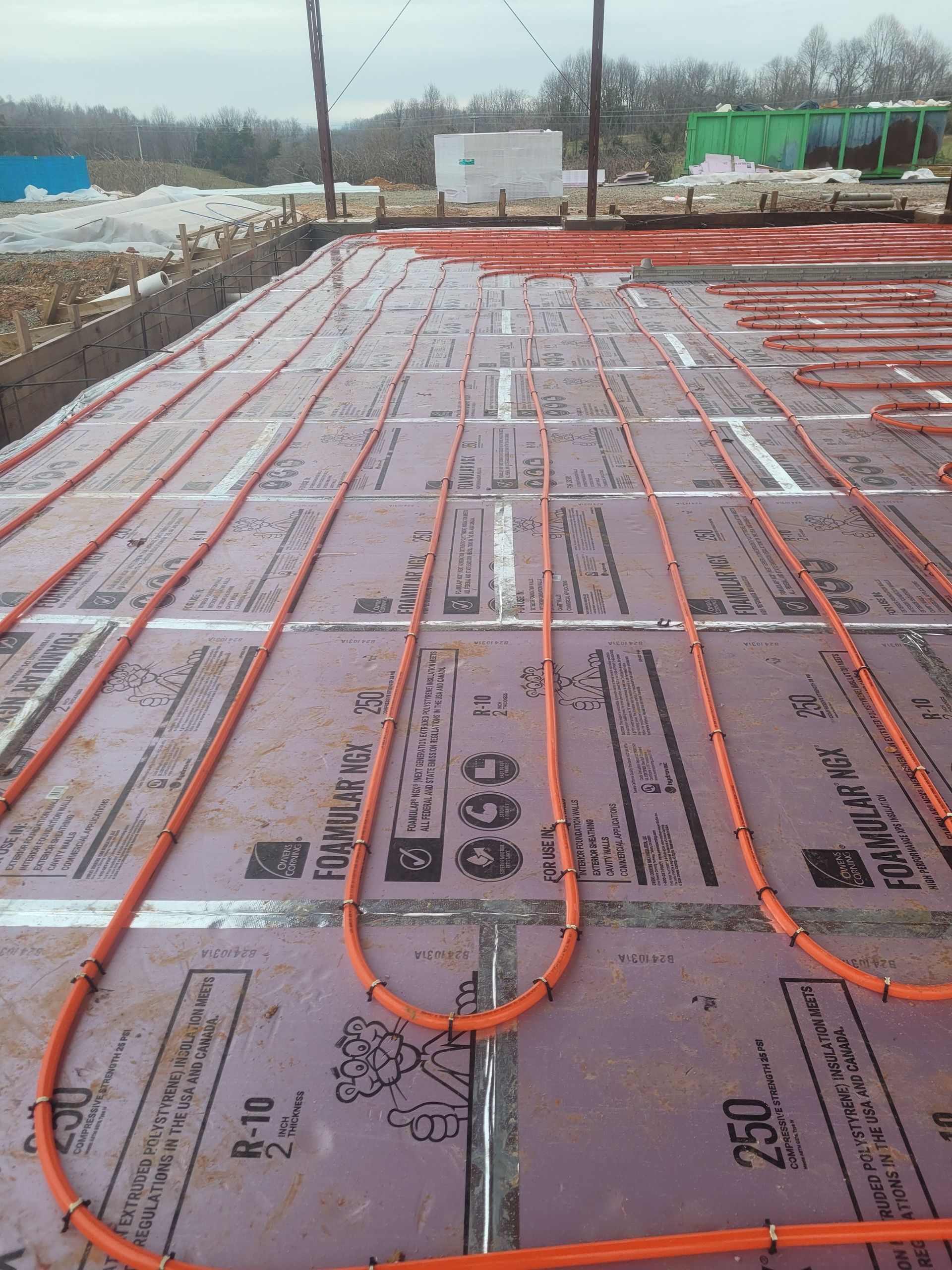 Orange tubing laid on purple insulation, likely for in-floor radiant heating, ready for concrete pour.