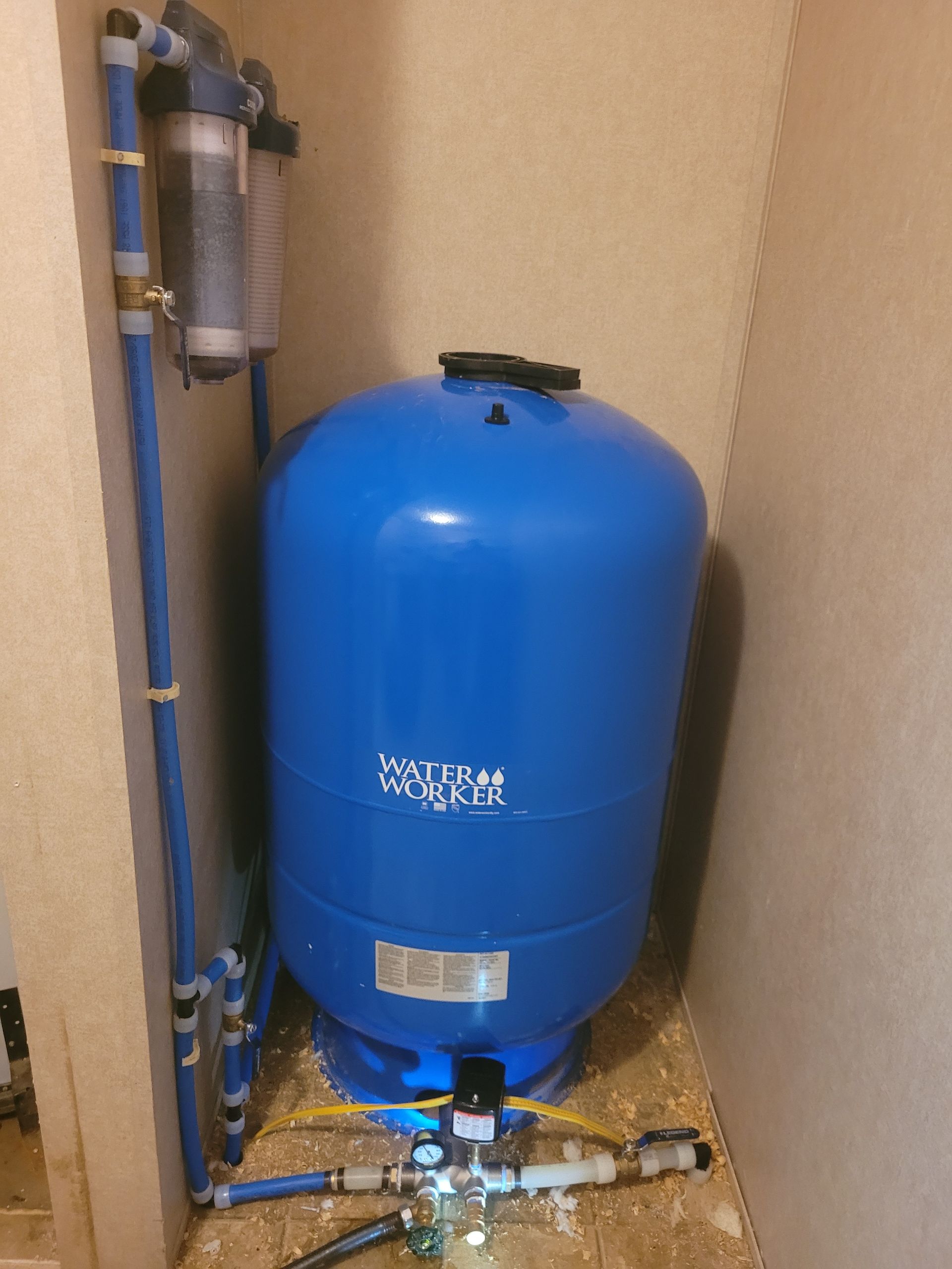 Blue water pressure tank with attached filters and pipes in a corner.