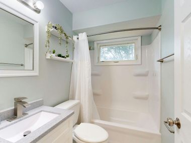 Bathroom with white fixtures, pale blue walls, and a small window.