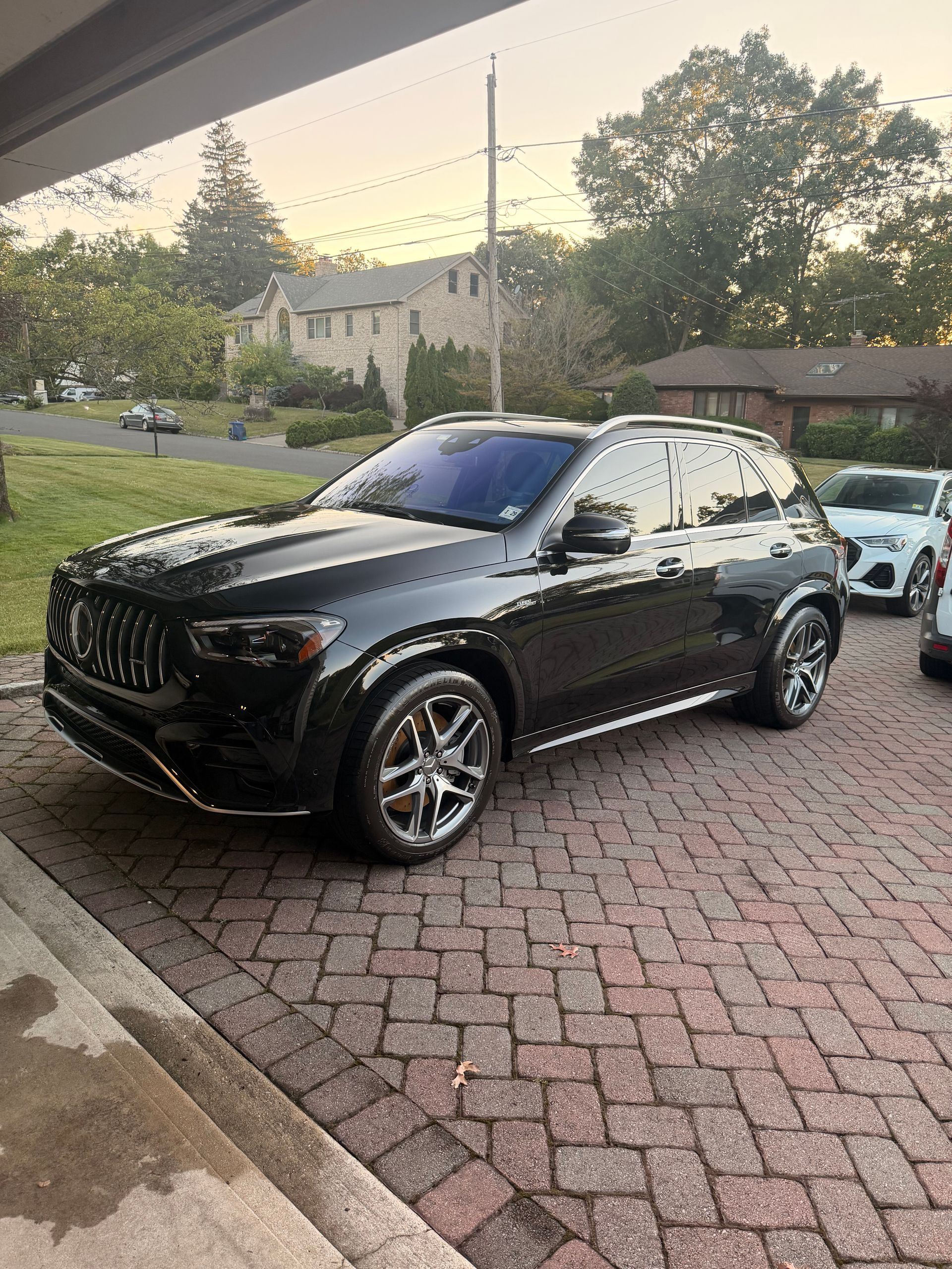 Black SUV parked on a brick driveway at dusk with trees and houses in the background