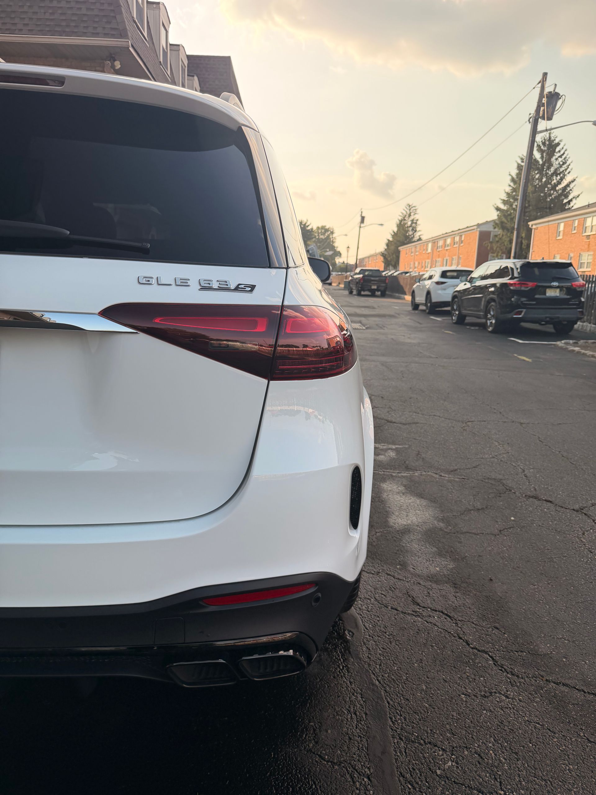 White SUV parked on a street at sunset, rear view with taillight and city traffic in the background
