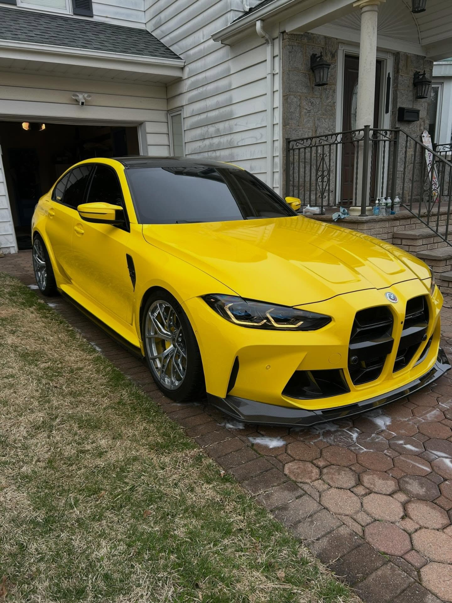 Yellow BMW parked in a driveway beside a white house and garage.