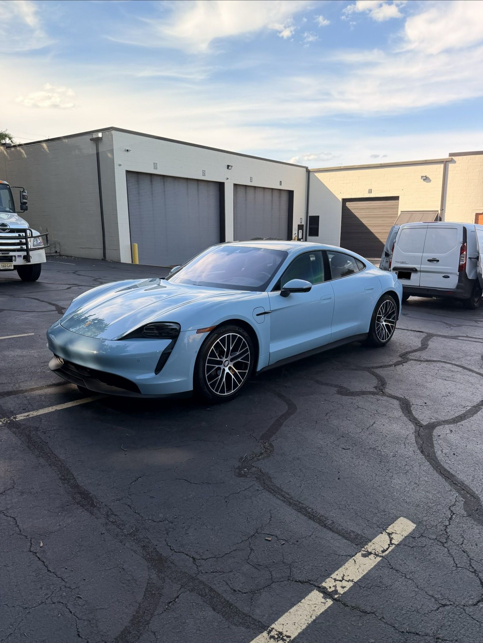 Light blue sports car parked in an industrial lot near garages and vans