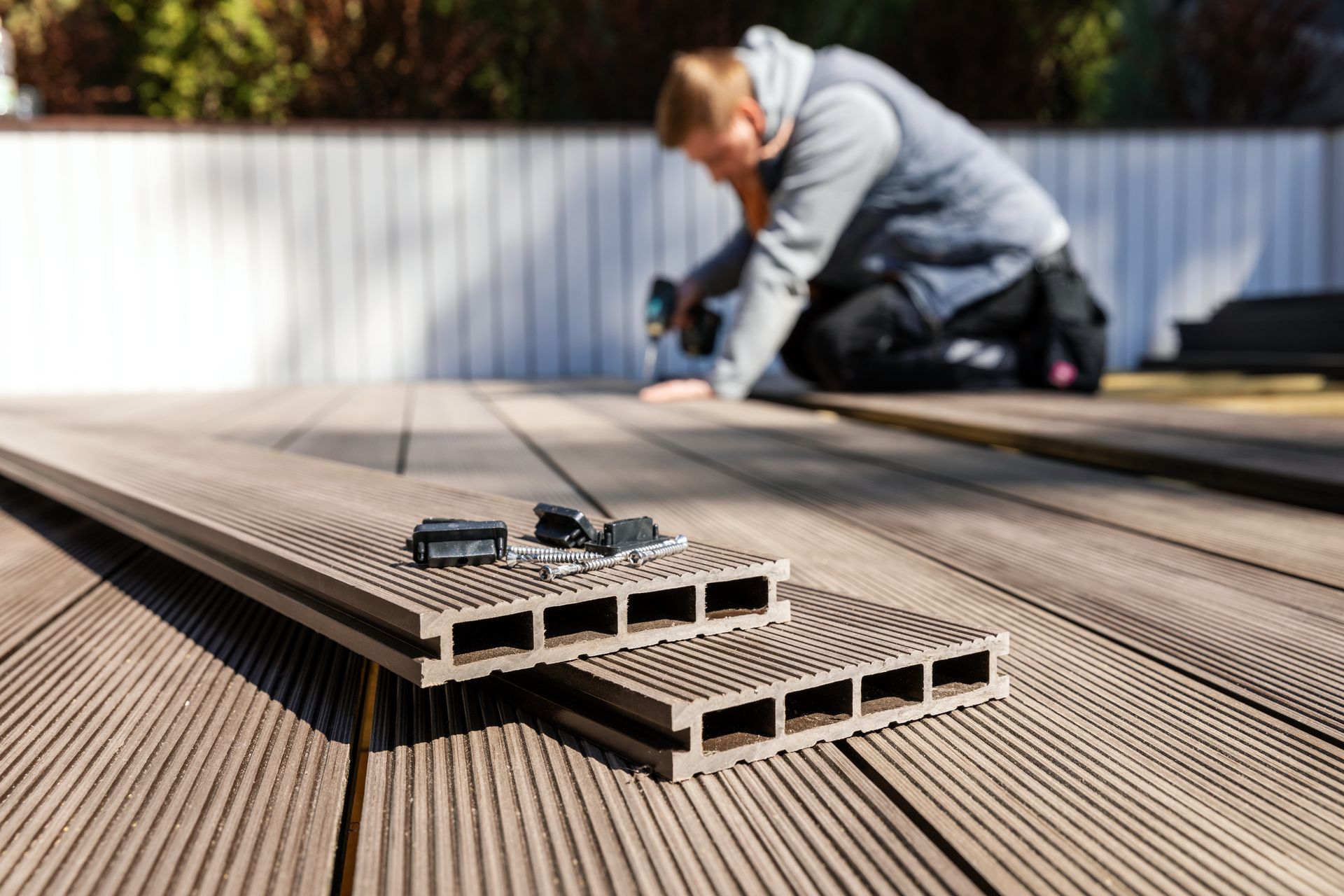 Un homme travaille sur une terrasse en bois avec une perceuse.