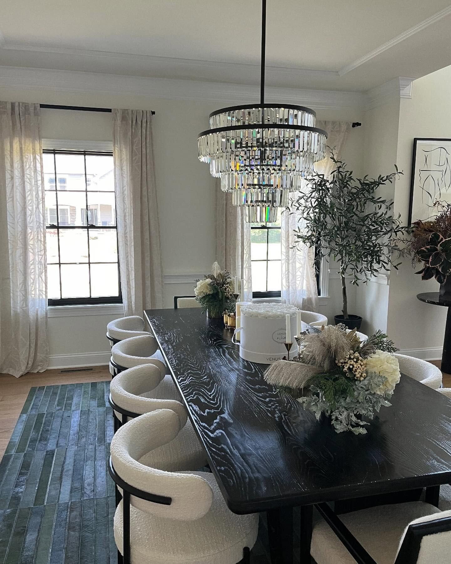 Elegant dining room with black table, cream chairs, crystal chandelier, and floral centerpiece.