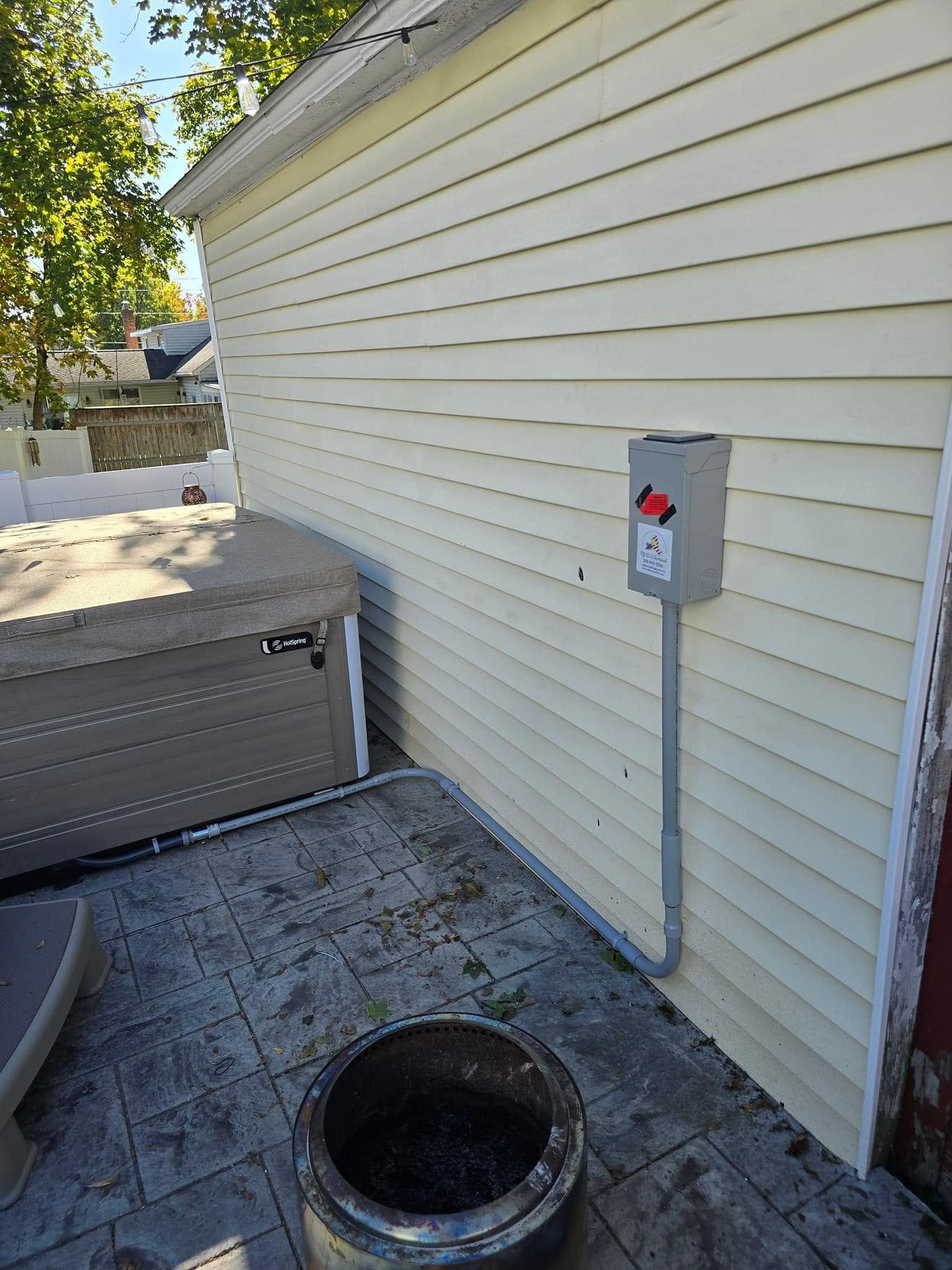 Outdoor utility area beside a house, with a sewer cleanout opening and electrical panel on the wall.