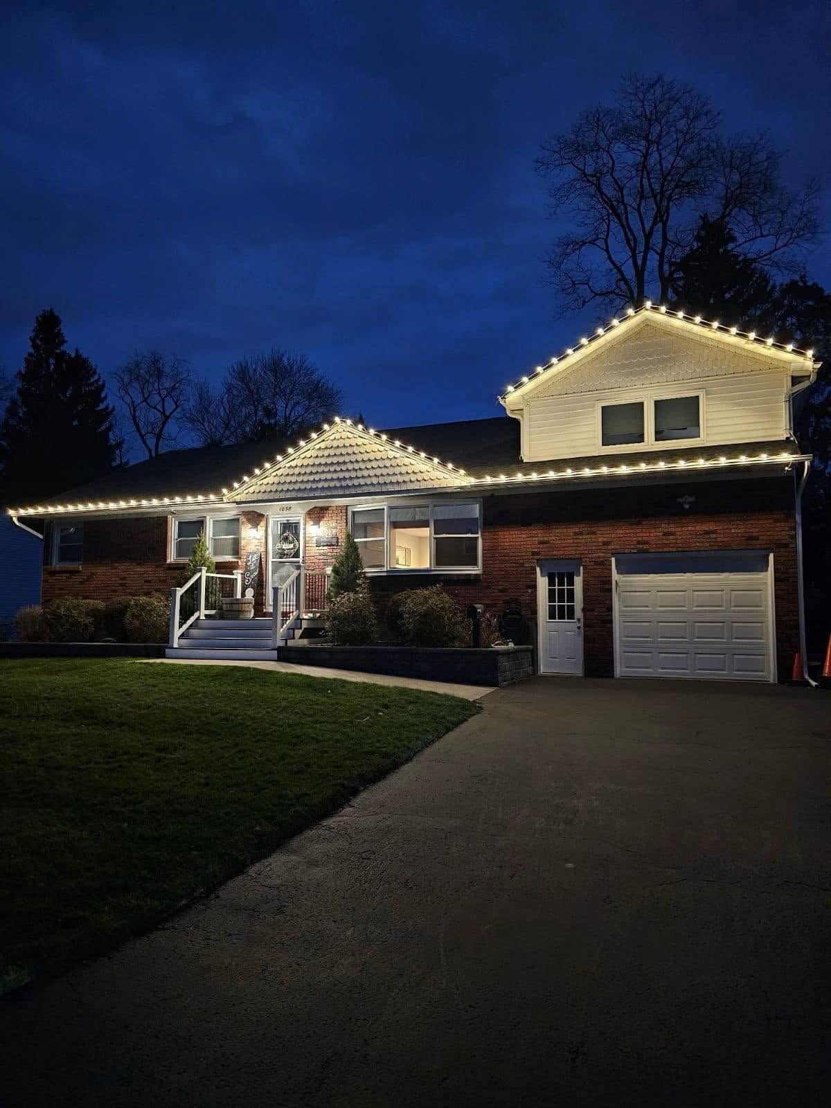 Suburban house at dusk with warm roofline lights and a driveway leading to the garage