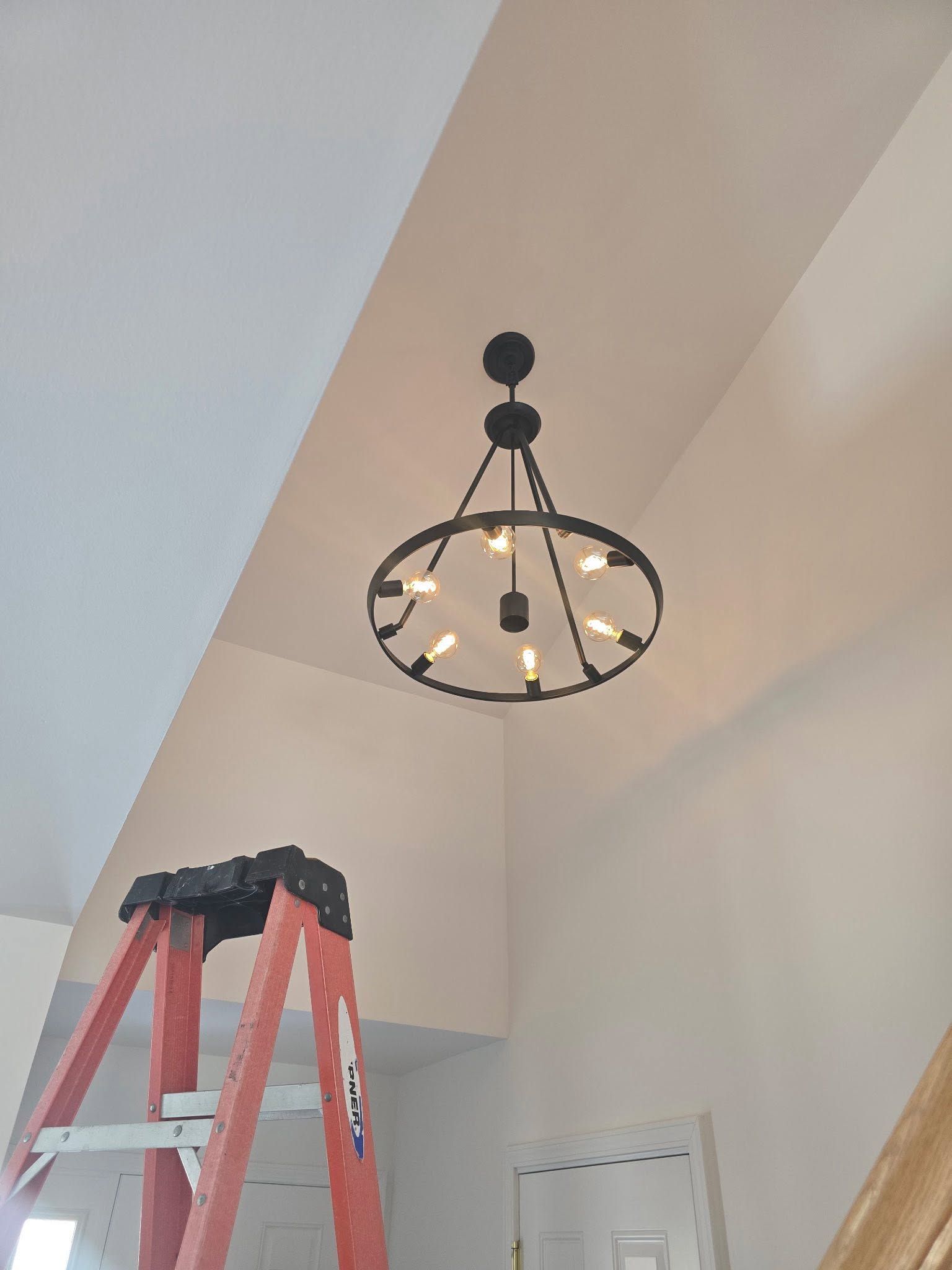 Ceiling chandelier above a red ladder in a room with sloped white walls