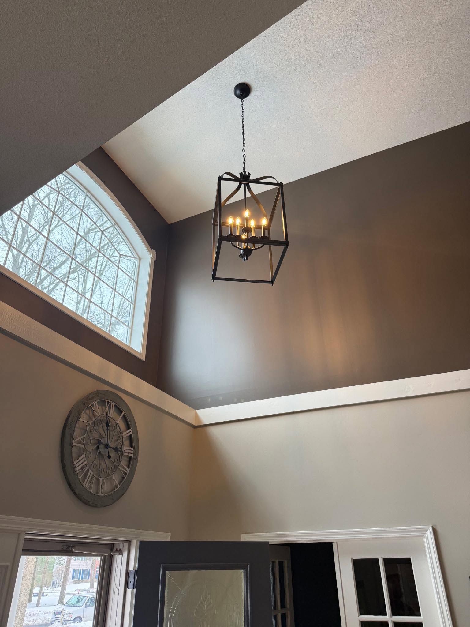 High-ceiling foyer with a hanging lantern, angled window, wall clock, and open front door.