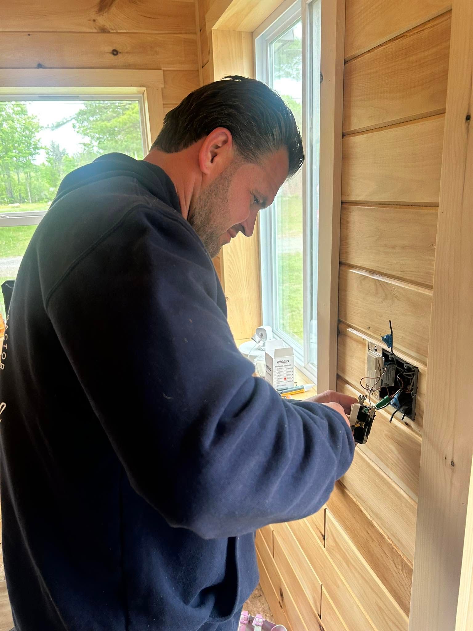 Man installing an electrical outlet in a wood-paneled room near a window