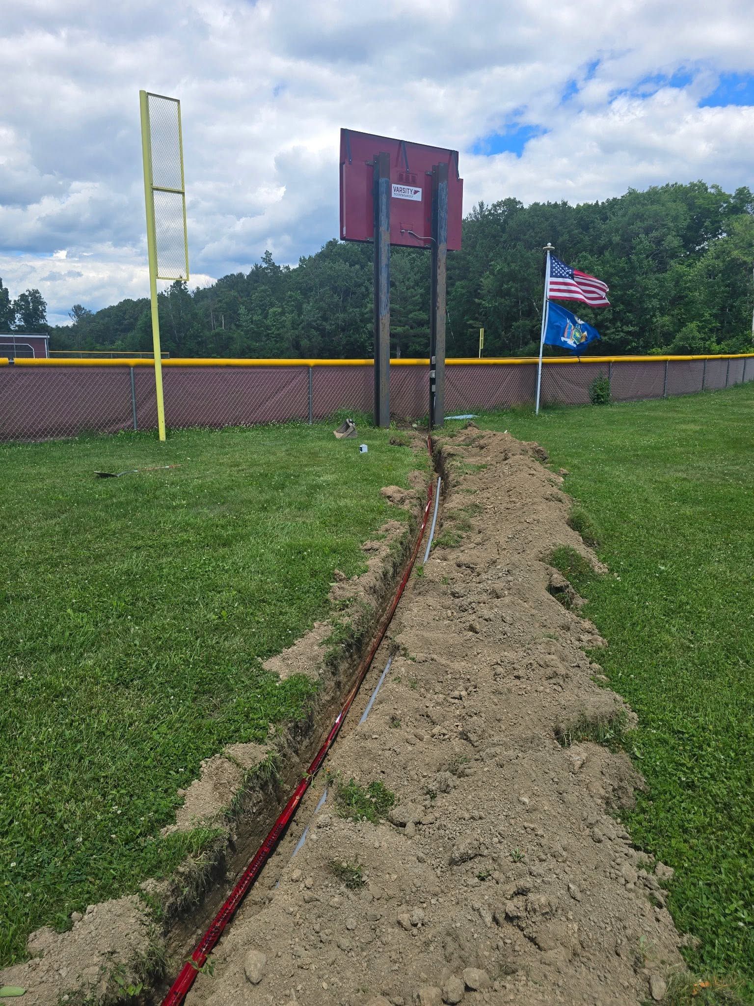 Rope-lined sandy path leading to a sign and flag by a brick wall under a cloudy sky