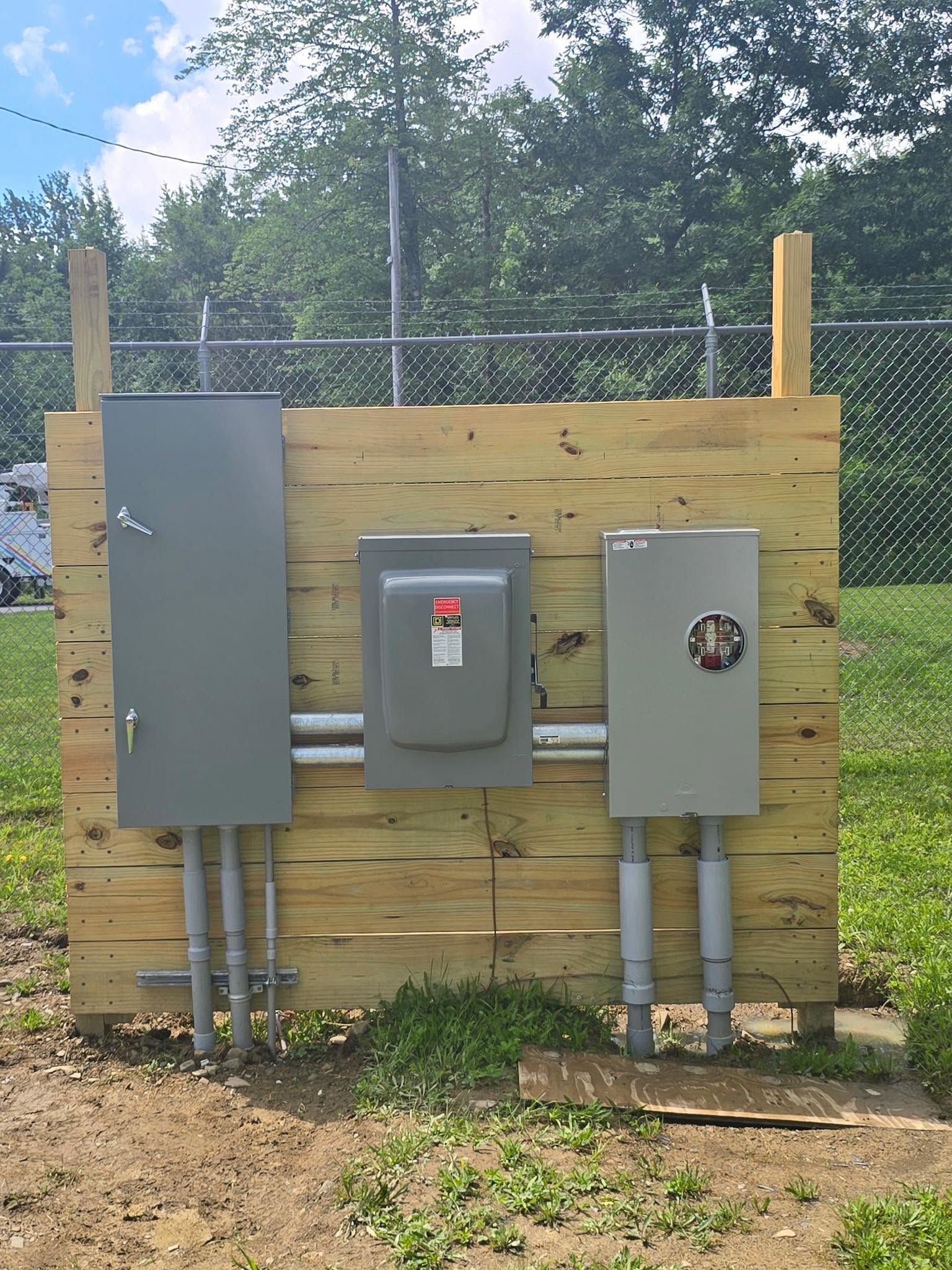 Three electrical utility boxes mounted on a wooden fence outdoors.