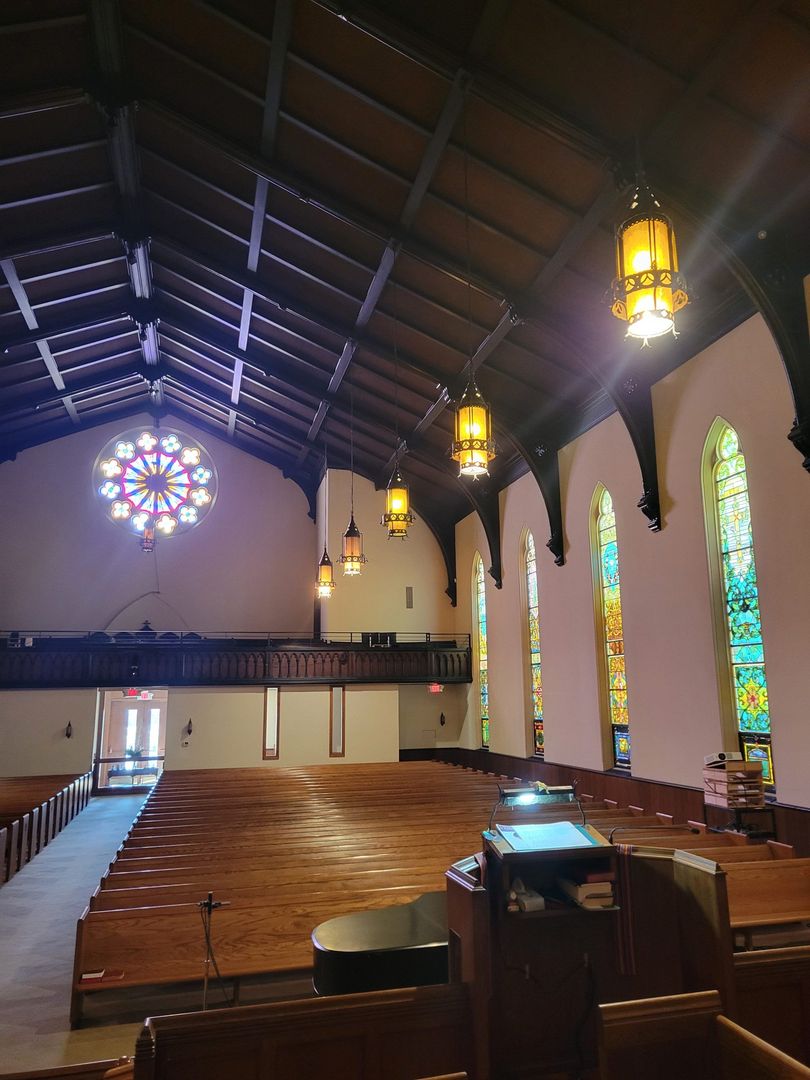 Empty church nave with stained-glass windows, hanging lanterns, and wooden pews beneath a vaulted ceiling